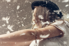 Two people holding hands, with feathers falling around their face.