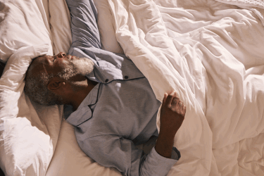 A mature man rouses in the early morning light, stretching as he wakes.