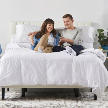 A man and a woman sitting up in bed using thier adjustable base.