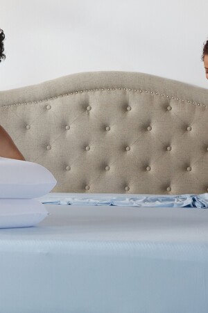 Two people making a bed together with light blue sheets. Two deluxe comfort cool pillows are on the corner of the bed.