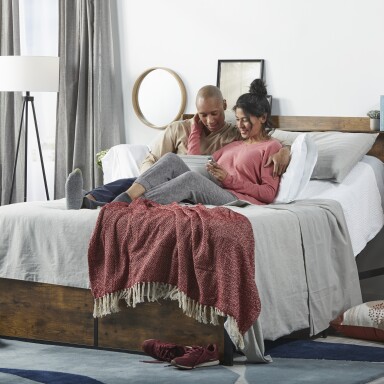 A couple laying on an adjustable bed looking at a tablet.