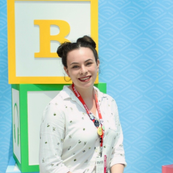 Alicia Hughes sitting down smiling at the camera against a blue backdrop.