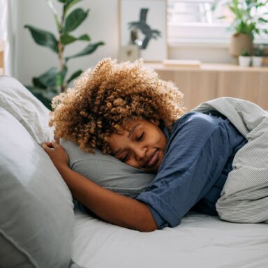 A black woman sleeping in bed hugging her pillow to her face.